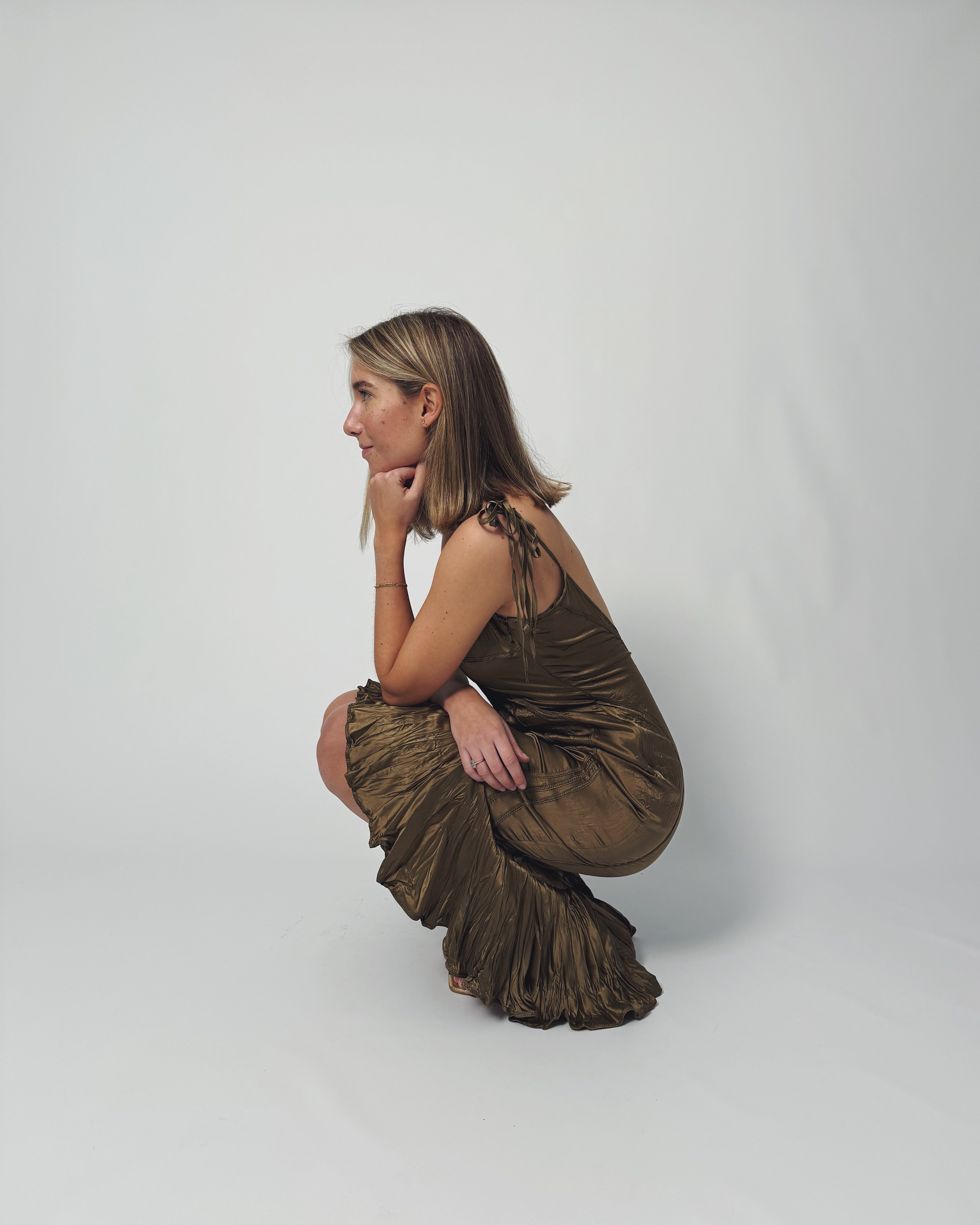 Woman in a brown dress sitting on the floor against a white background