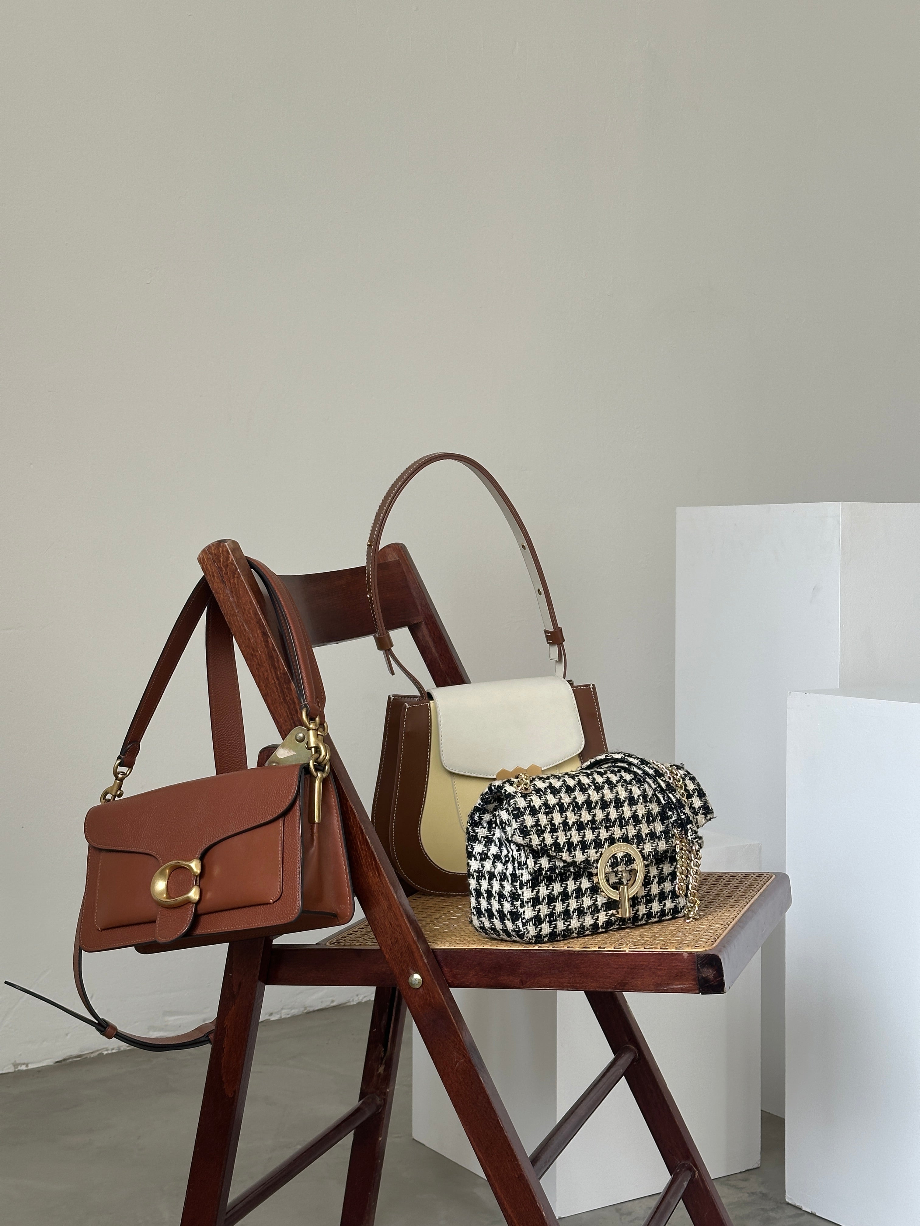 Brown leather handbag with gold hardware on a chair, houndstooth patterned bag in the background.